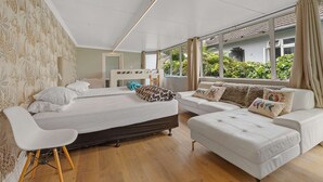 Een moderne slaapkamer met een groot bed, een bank en een stoel. Er zijn grote ramen met gordijnen, en uitzicht op groen buiten.