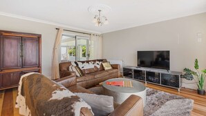 Een woonkamer met een leren bank, een ronde salontafel, een televisie en een kast met planten.