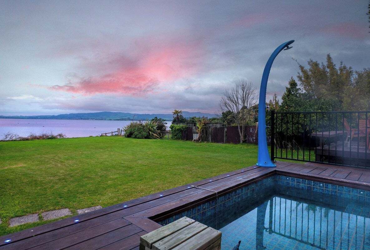 A swimming pool with a curved edge, surrounded by a wooden deck and a metal fence.
