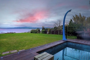 A swimming pool with a curved edge, surrounded by a wooden deck and a metal fence. - Lakefront Rotorua in Town (Rotorua Township)