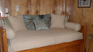 A wooden sofa bed with a textured beige cover, two side tables, and a framed picture on the wall.