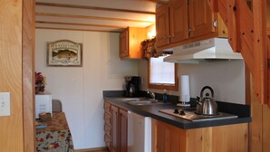 A compact kitchen with wooden cabinets, a refrigerator, a sink, and a kettle on the countertop.