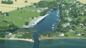 An aerial view of a marina with boats docked along a narrow waterway, surrounded by residential properties and green fields.