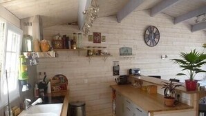 A kitchen with a wooden countertop, a sink, and a trash can. There are shelves with various items and a clock on the wall.