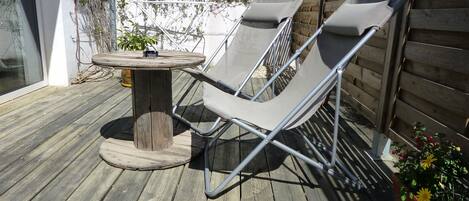 Eine Holzterrasse mit einem Metalltisch und zwei grauen Loungestühlen.