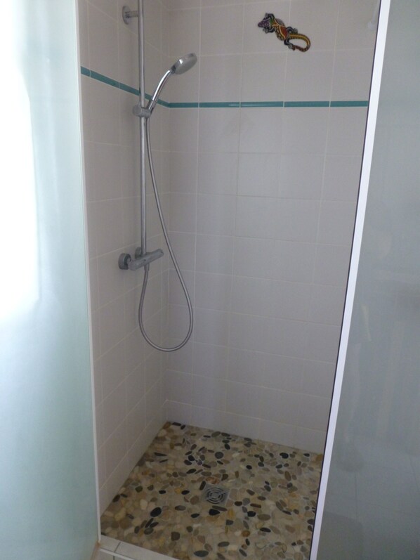 A shower with a handheld showerhead and a rain shower head, tiled walls, and a pebble-patterned floor.