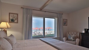 Habitación de hotel con una cama grande, una silla, un aparador y vistas a la playa con sombrillas.