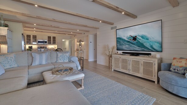 Una sala moderna con un televisor de pantalla plana grande, un sofá, una mesa de centro y un comedor al fondo.