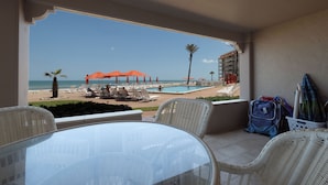 Un balcón con vista a una playa, piscina y palmeras.