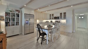Una cocina moderna con armarios blancos, una isla central con asientos y una estantería empotrada.