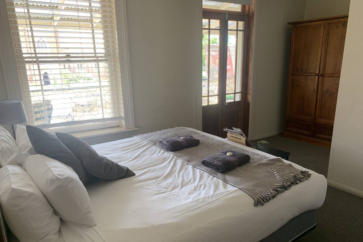 A neatly made bed with white linens and two pillows, a striped blanket, and two folded towels with a small round object on each.