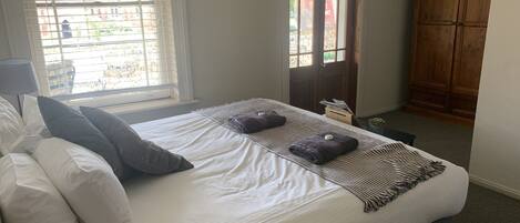 A neatly made bed with white linens and two pillows, a striped blanket, and two folded towels with a small round object on each.