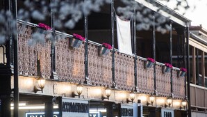 A building facade with ornate metal railings, multiple signs including "ACCOMMODATION" and "FOOD," and hanging flower baskets.