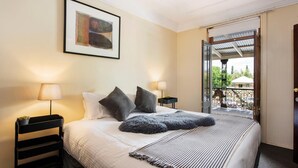 A hotel room with a bed, two bedside lamps, a framed artwork, and a balcony with a wrought iron gate.