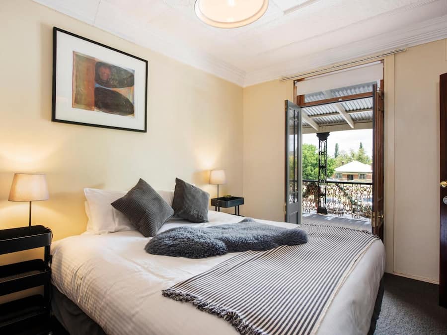 A hotel room with a bed, two bedside lamps, a framed artwork, and a balcony with a wrought iron gate.