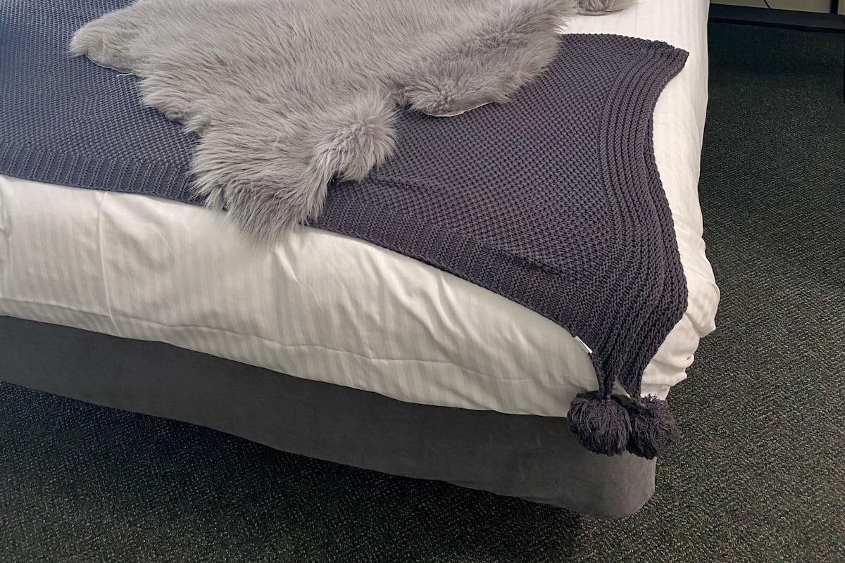 A neatly made bed with a fluffy gray blanket and a dark blue pillow.