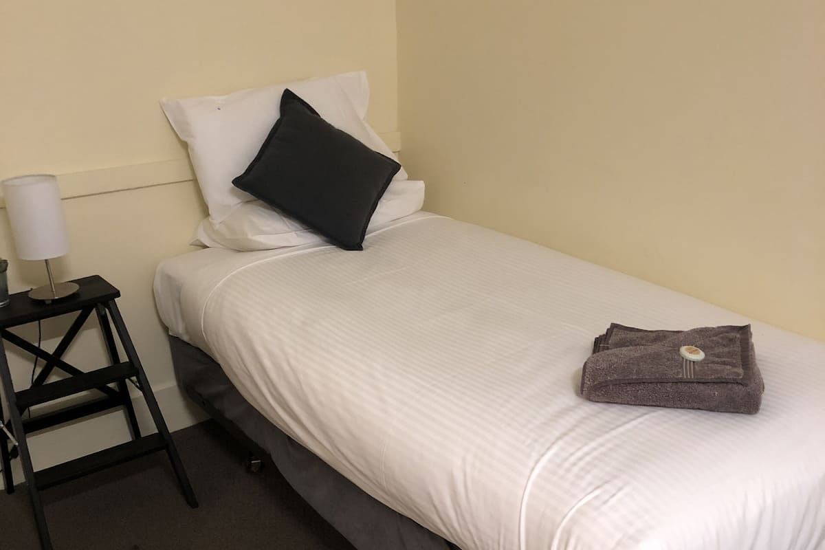 A single bed with white bedding, a black pillow, and a folded towel on the right side.