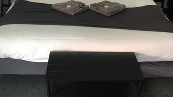 Una cama bien hecha con ropa de cama blanca y negra, dos almohadas y dos toallas dobladas sobre la cama. Al pie de la cama hay un banco negro.