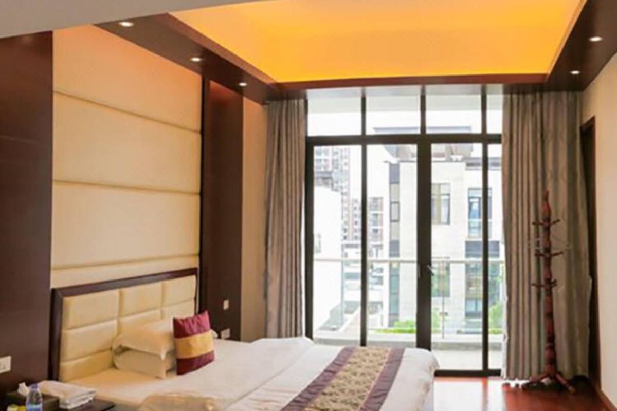 Een hotelkamer met een groot bed, een nachtkastje, een raam met gordijnen en uitzicht op gebouwen.