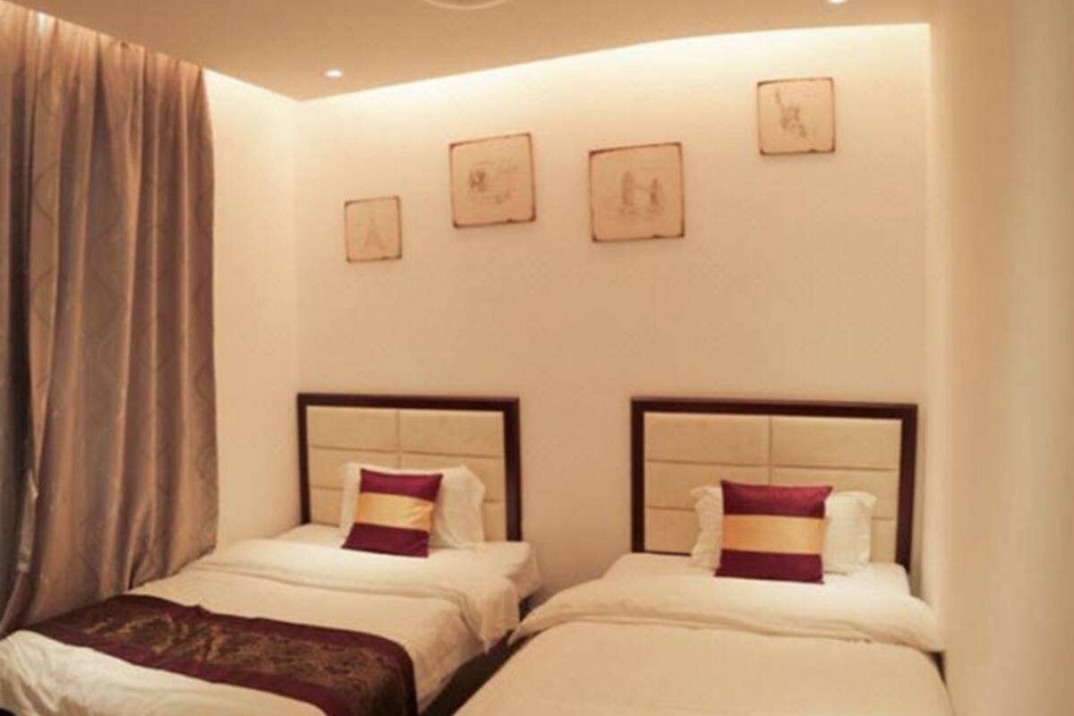 Een hotelkamer met twee bedden, elk voorzien van een hoofdbord, wit beddengoed en een decoratief kussen. Boven de bedden hangen drie ingelijste foto’s.