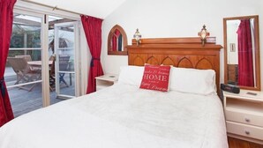 A bedroom with a large bed, a wooden headboard, a nightstand, a mirror, and a sliding glass door leading to an outdoor area with a table and chairs.
