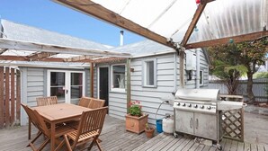 A covered patio with a wooden table and chairs, a grill, and potted plants.