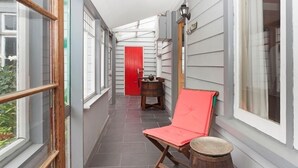 A narrow corridor with a red door, a wooden chair, and a small table with a barrel.