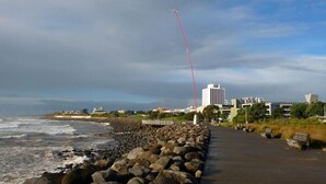 A coastal walkway with a rocky barrier, a red pole, and buildings in the background. - Fab Studio Plus!!- Pukekura Park/CBD right there (New Plymouth)