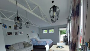 A modern room with a wooden dining table, a bed with a patterned duvet, a grey sofa, and a wall with framed pictures. - Fab Studio Plus!!- Pukekura Park/CBD right there (New Plymouth)