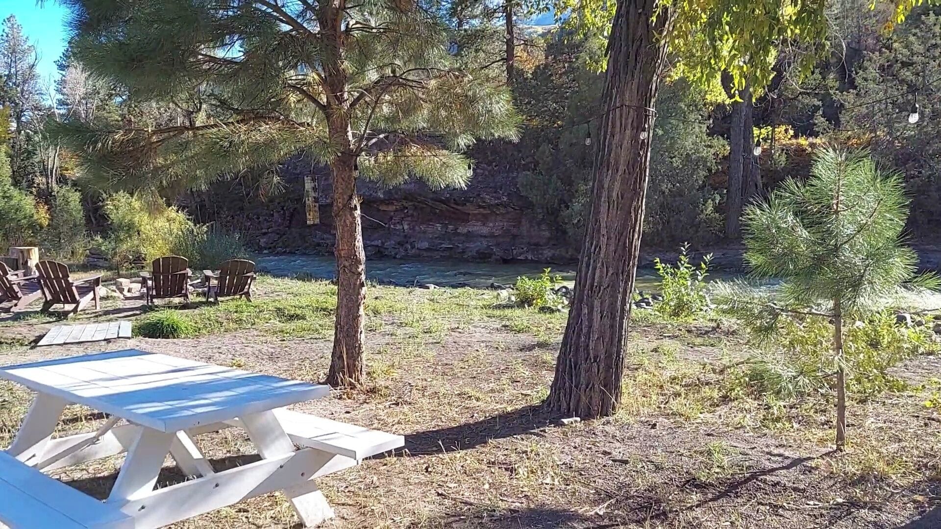A picnic table in a forested area with chairs and a river in the background.