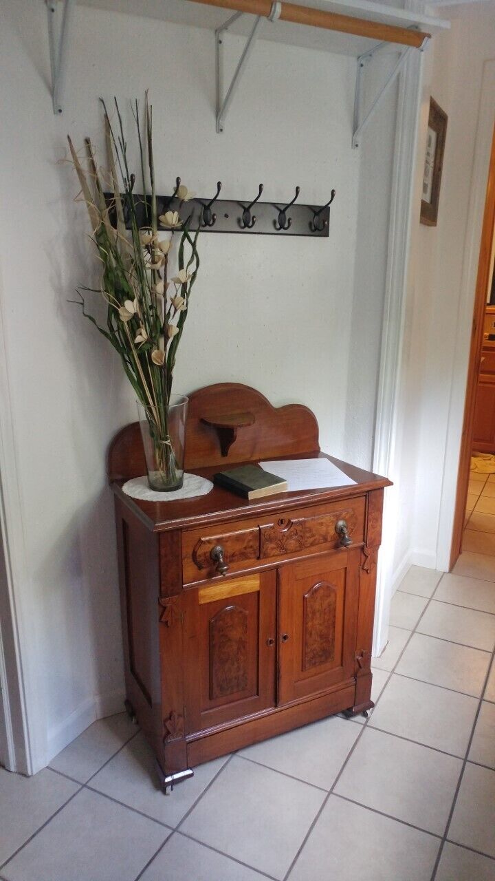 A wooden cabinet with a vase of dried flowers on top, a book, and a coat rack with hooks on the wall.