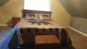 A bedroom with a bed, a nightstand, a window, and a sloped ceiling.