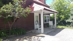 A wooden cabin with a porch, two rocking chairs, and a small garden area. - Cabin by the river, room to roam. Close access to all the best. 30+ days (Ridgway)