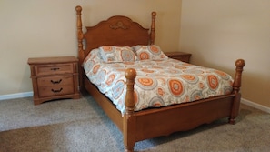 Ein Bett mit Holzbettgestell und einem gemusterten Bettbezug, ein Nachttisch mit Schubladen und ein Teppichboden.