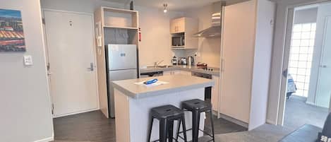 Een moderne keuken met een centraal eiland, barkrukken en uitzicht op een kamer met een deur.