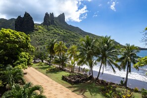 A pathway leading to a beach with palm trees and a mountainous backdrop.