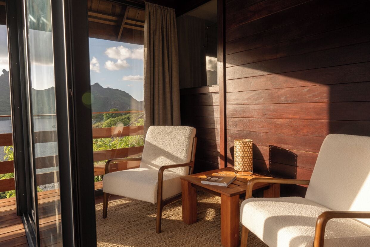Ein Zimmer mit zwei Stühlen, einem Tisch und Bergblick durch große Fenster.
