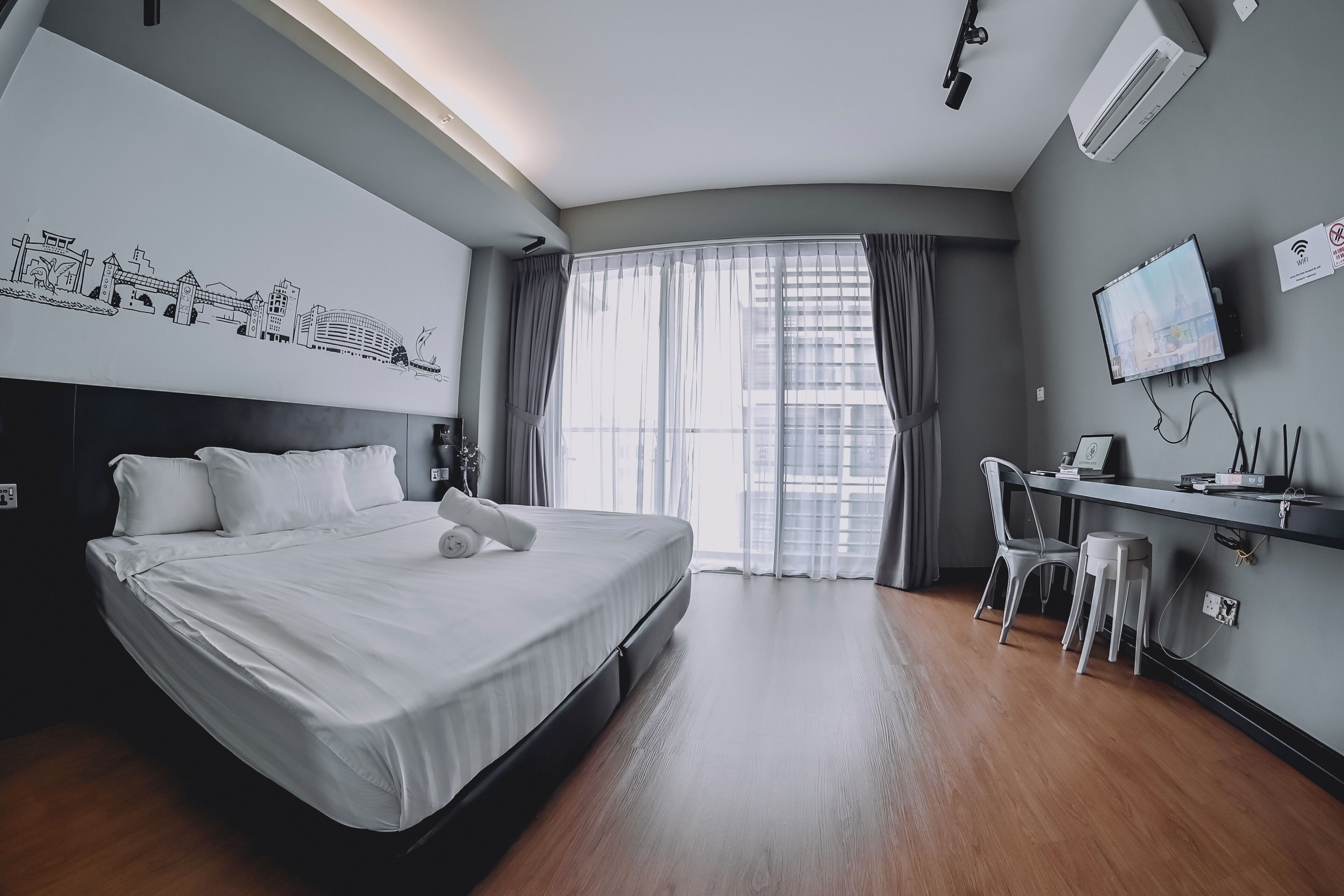 Une chambre d’hôtel avec un grand lit, un bureau avec une chaise, une télévision et une fenêtre avec des rideaux.