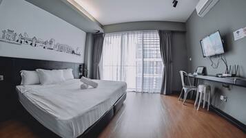 Une chambre d’hôtel avec un grand lit, un bureau avec une chaise, une télévision et une fenêtre avec des rideaux.