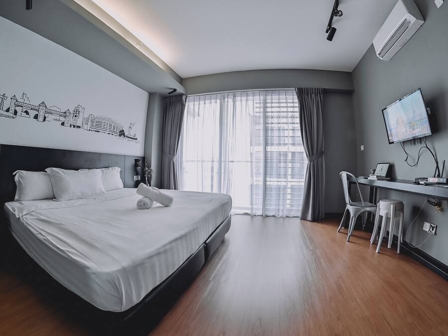 Une chambre d’hôtel avec un grand lit, un bureau avec une chaise, une télévision et une fenêtre avec des rideaux.