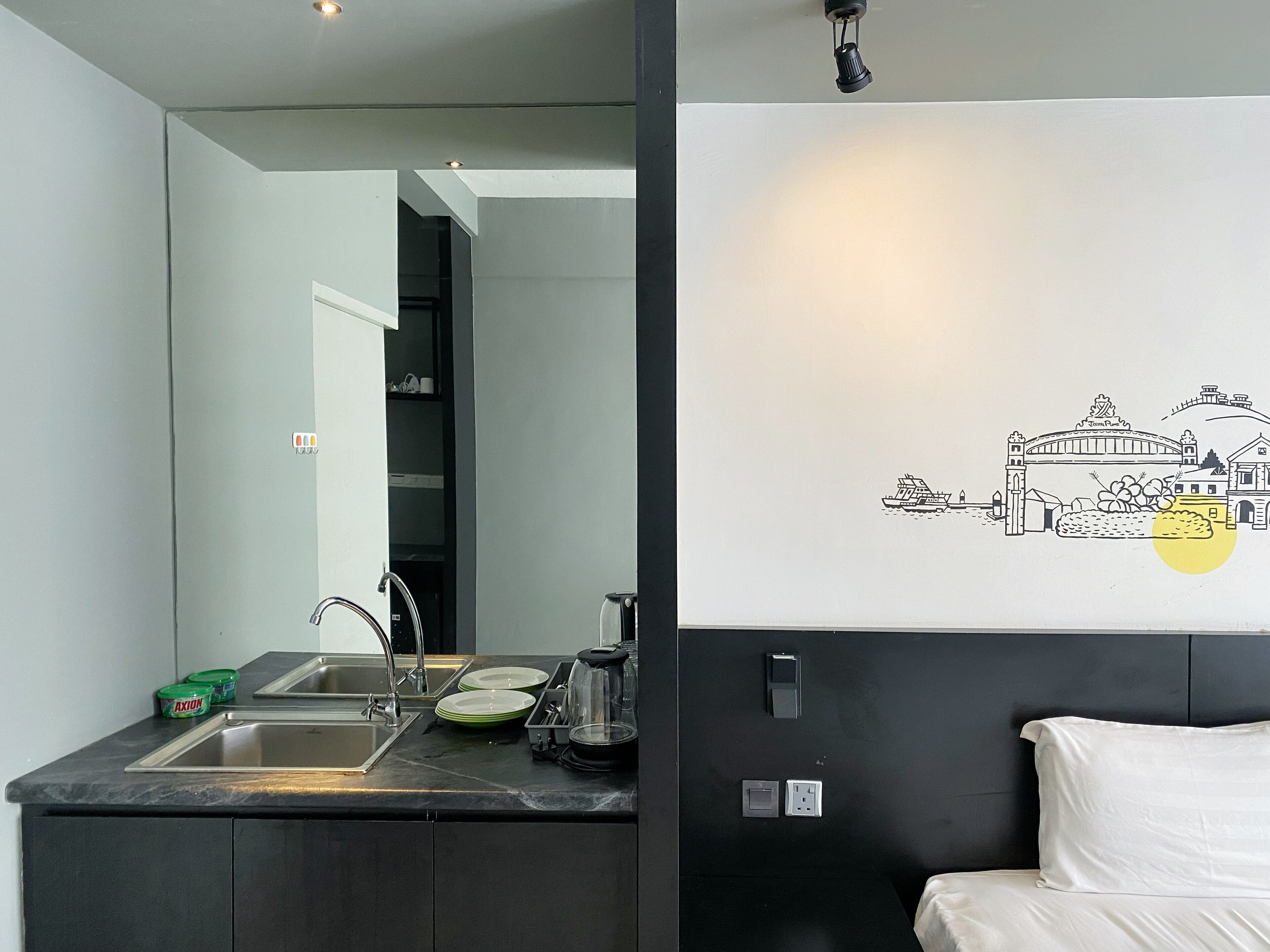 Cocina moderna con lavaplatos, estufa y armarios. Hay un aplique de pared y un cuadro con una escena urbana.