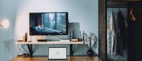 A modern room with a TV on a wooden shelf, a laptop on a table, and a clothing rack with hanging clothes.