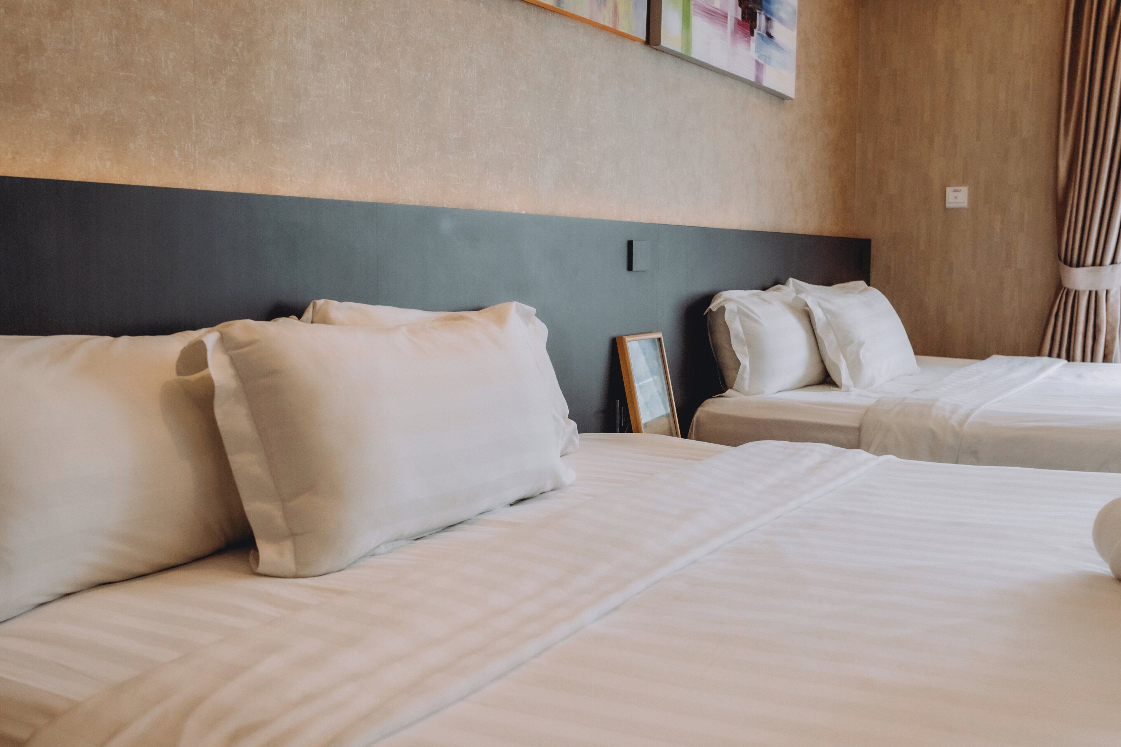 Quarto de hotel com duas camas, cada uma com roupa de cama e almofadas brancas.
