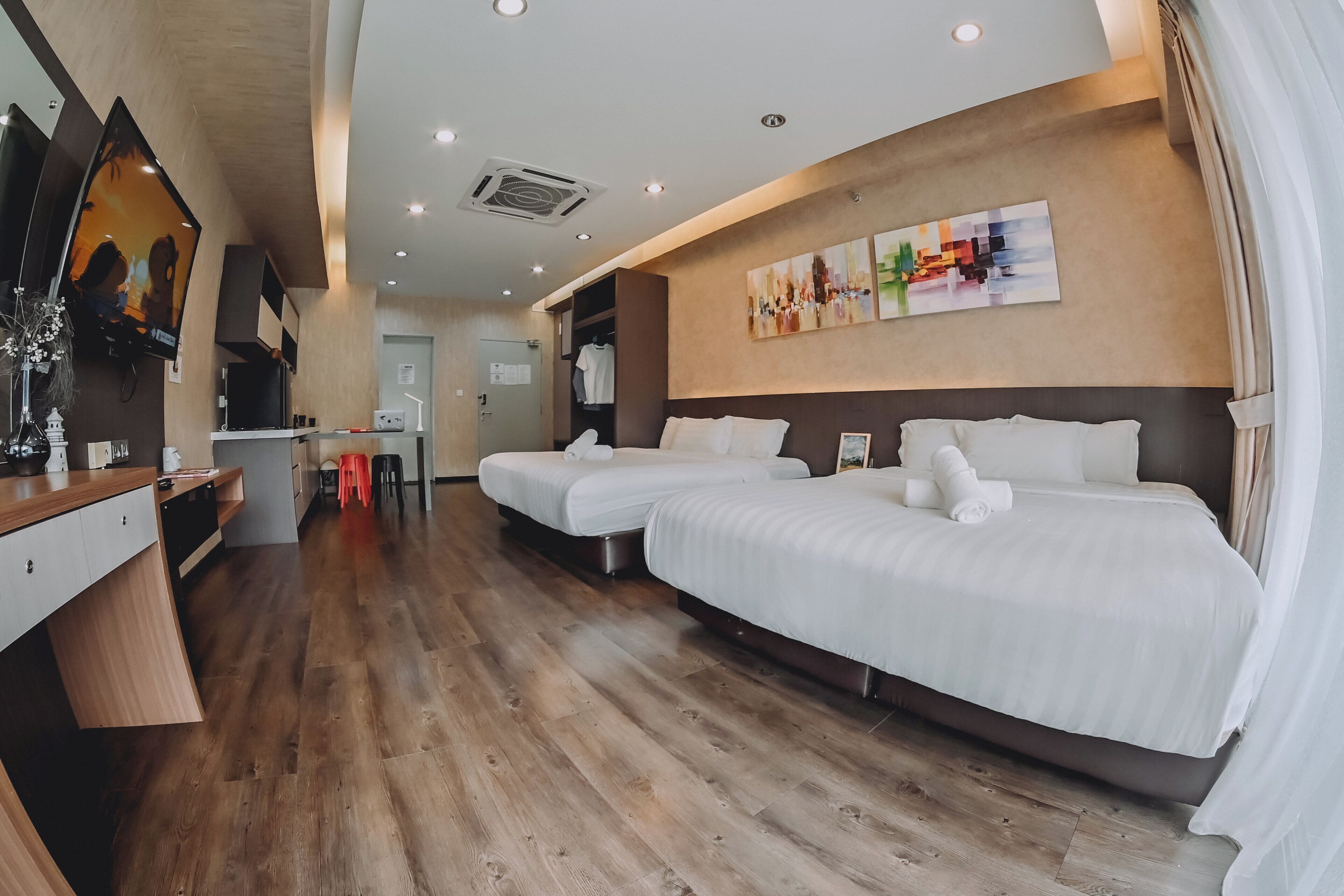 A hotel room with two beds, a wooden floor, a TV, and a painting on the wall.
