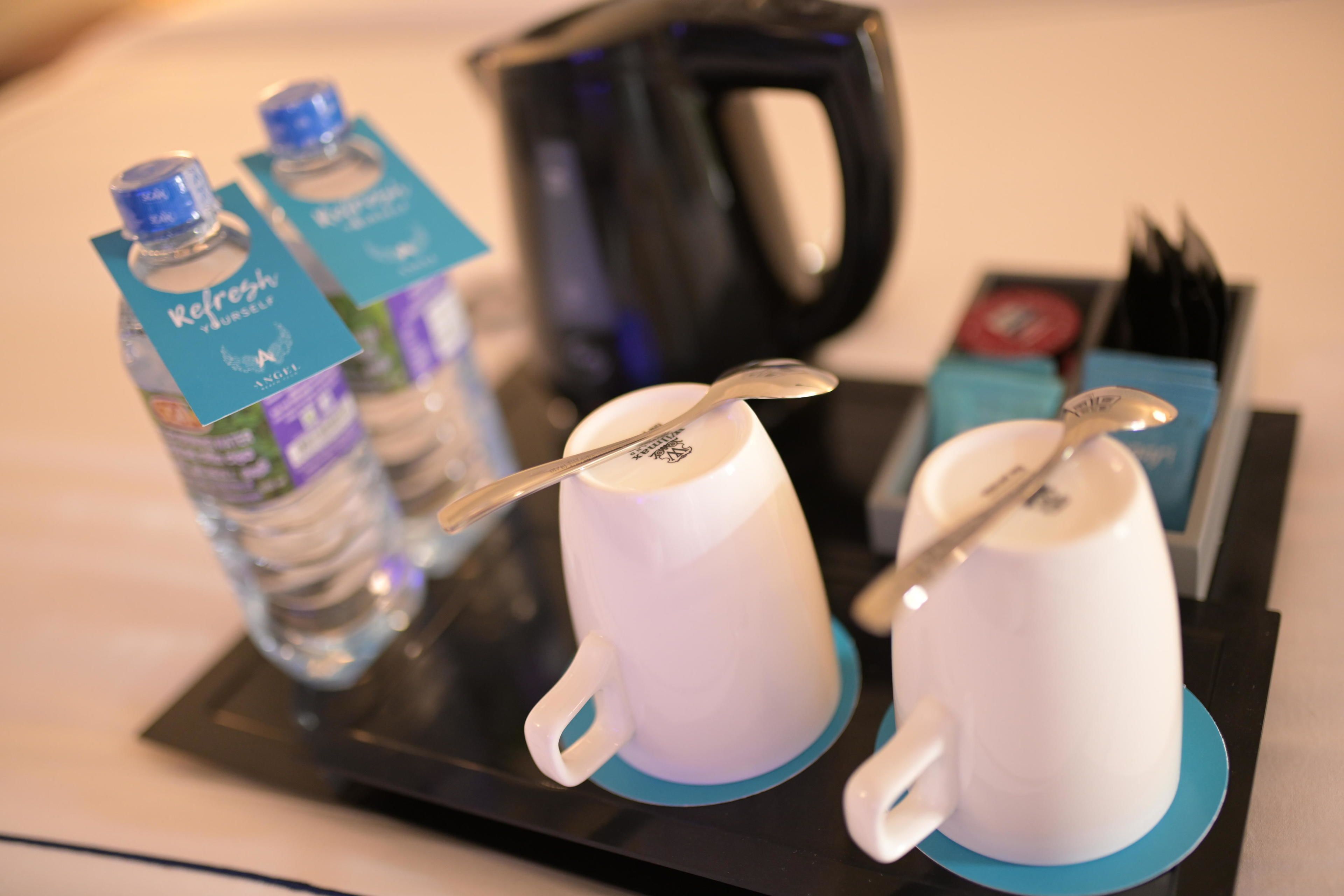 A tray with two white mugs, a spoon, and two bottles of water with labels.