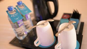 A tray with two white mugs, a spoon, and two bottles of water with labels.