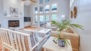 A spacious living room with a fireplace, a large window, a ceiling fan, and a potted plant.