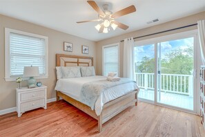 A bedroom with a bed, a nightstand, a ceiling fan, and a large window with a view of the outdoors. - Lovely Folly Beach Home Just Steps to the Beach! (Folly Beach)