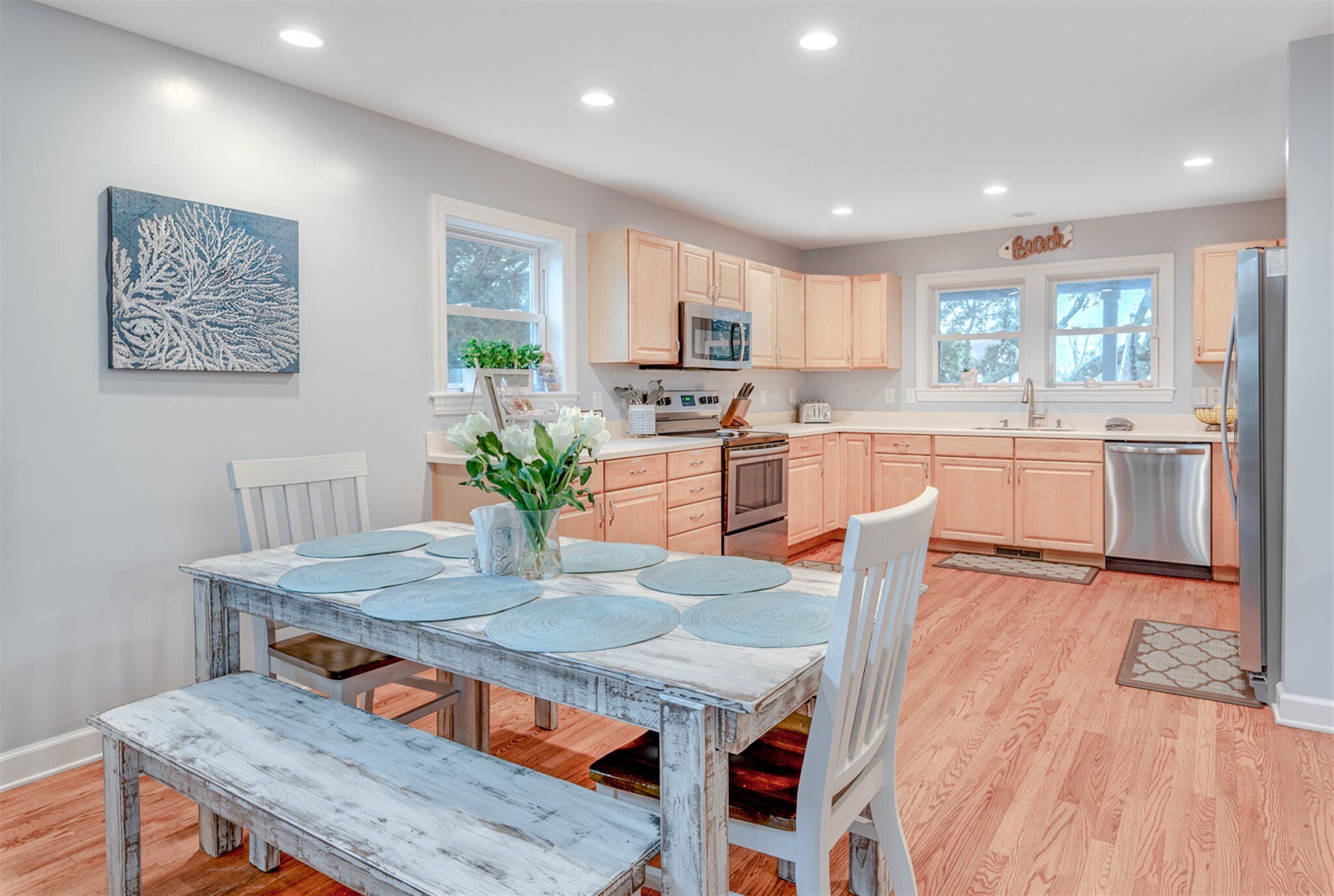 A modern kitchen with light wood cabinets, a central island, and a dining area with a rustic table.