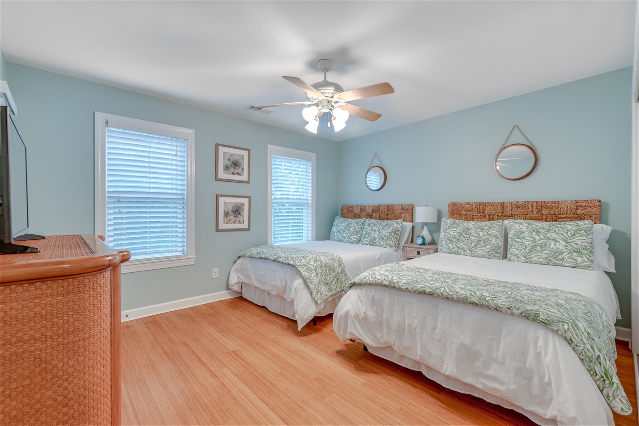 A bedroom with two beds, a ceiling fan, and a wooden floor.